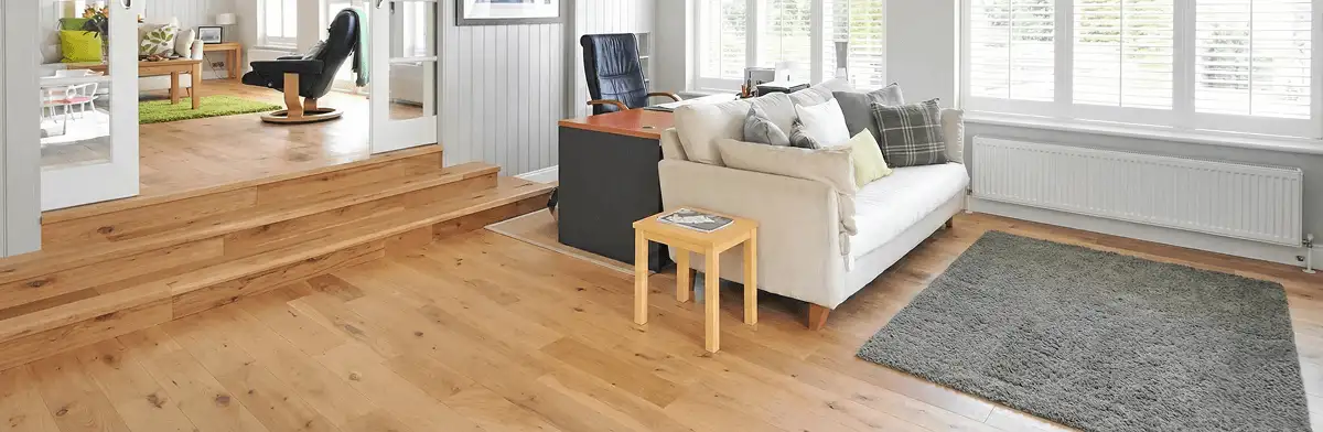 A modern living room with professionally installed laminate flooring, a beige sofa, a small side table, a gray rug, and large windows with white shutters in Gilbert, AZ